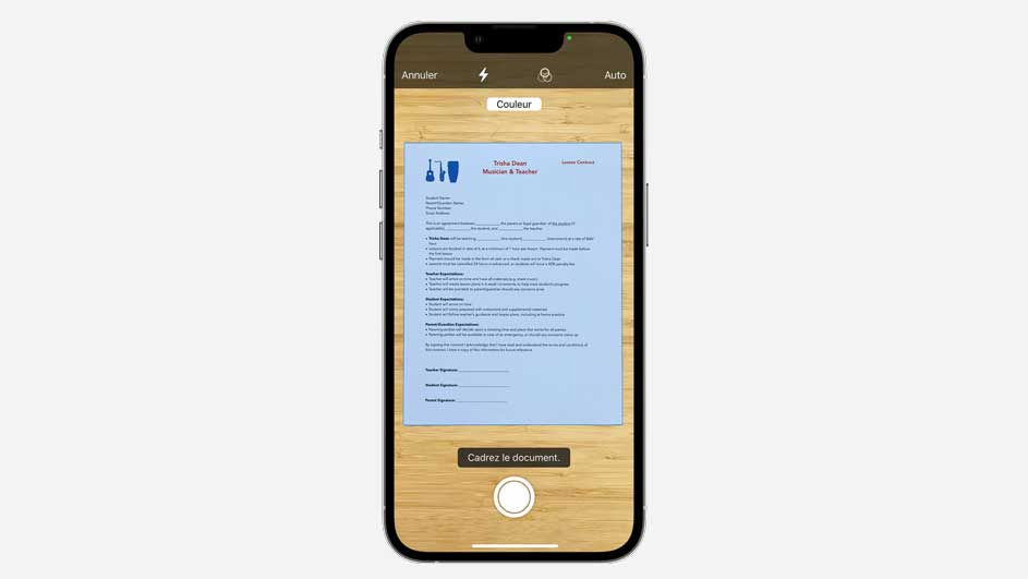 Un smartphone affiche un document bleu sur un fond en bois, avec des options de scan en haut et un bouton de capture en bas.