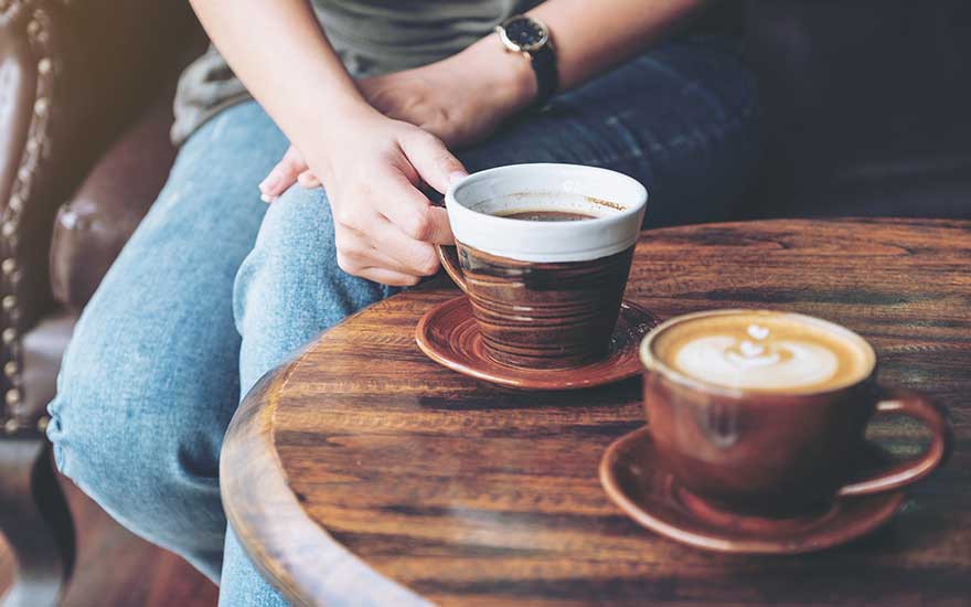 Deux tasses sur une table en bois. Une tasse contient du café noir, l'autre un latte avec un motif.