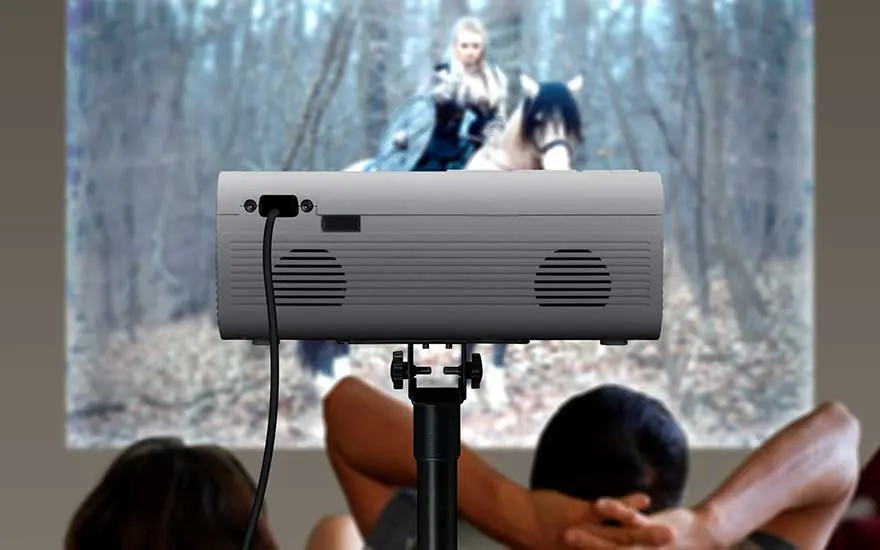 Un projecteur sur trépied diffuse un film pendant que deux personnes regardent ensemble, détendues.