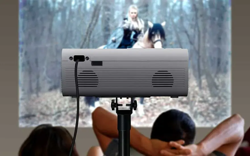 Un projecteur sur trépied diffuse un film pendant que deux personnes regardent ensemble, détendues.