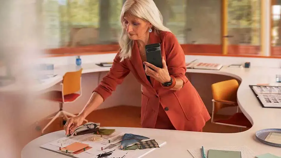 Een koraalkleurige blazer, een telefoon en staaltjes op een witte tafel. Een oranje stoel staat achter de tafel.
