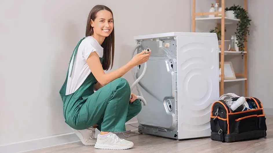 A white washing machine is being repaired. A black and orange toolbox is on the floor next to it.
