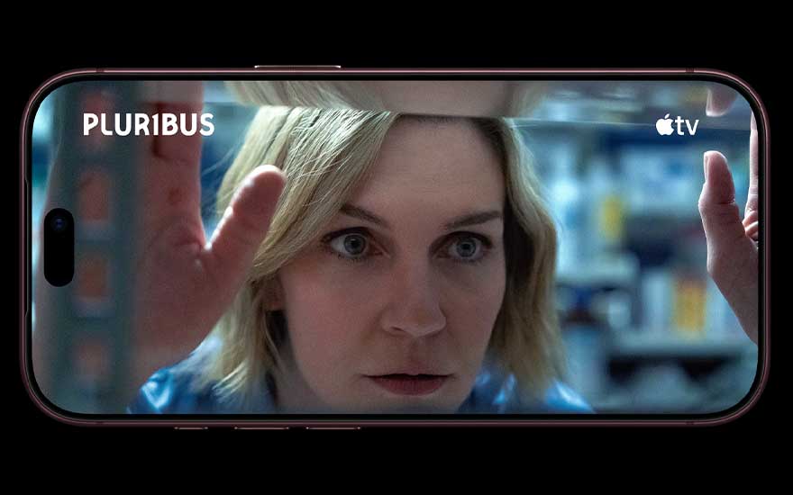 Een smartphone in liggende stand toont een close-up van een blonde vrouw, met de teksten “PLURIBUS” en “apple tv” bovenaan.