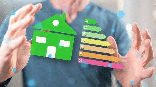 Een groene huisvorm en energie-efficiëntielabel (A-G) zweven tussen twee handen tegen een vage blauwe achtergrond.