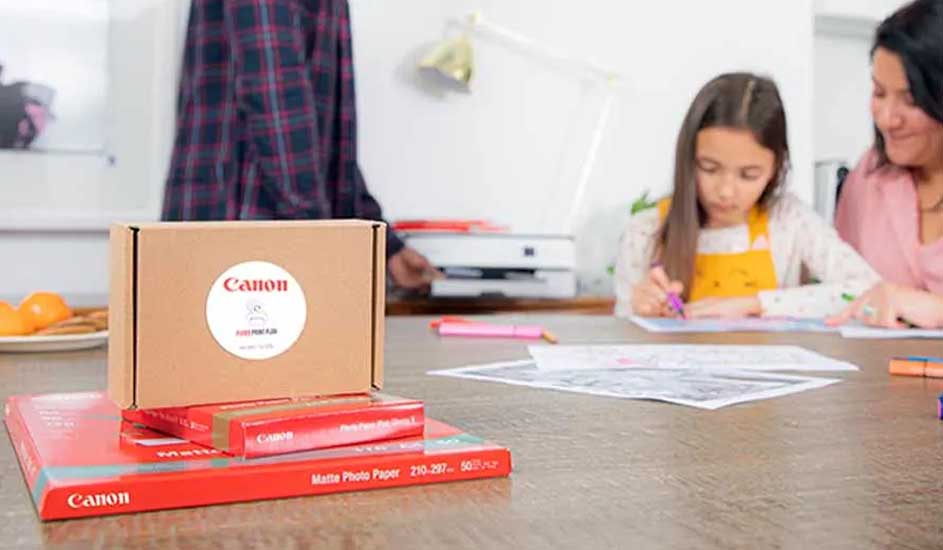 Boîte marron Canon sur papier photo rouge. Imprimante blanche en arrière-plan, sur une table avec des marqueurs et des dessins.