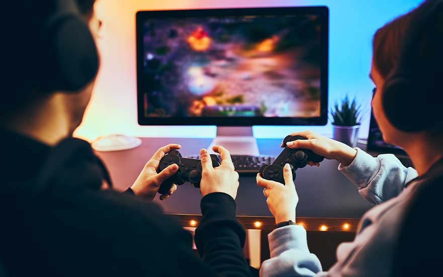 Two people wearing headphones hold controllers, playing video games together on a brightly lit computer screen