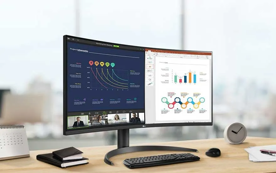 Écran avec graphiques et visioconférence sur bureau avec clavier, souris, agenda, horloge et bloc-notes.