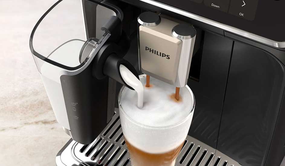A Philips coffee machine is frothing milk into a glass of coffee. It stands on a metal drip tray, with a milk container and control buttons visible.