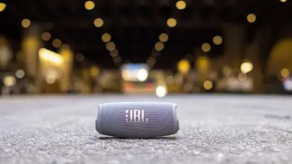 Grijze JBL-luidspreker op een grijze ondergrond, met vage stadslichten op de achtergrond.