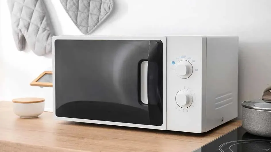 Micro-ondes blanc avec porte noire sur un comptoir en bois, avec des mitaines au mur.