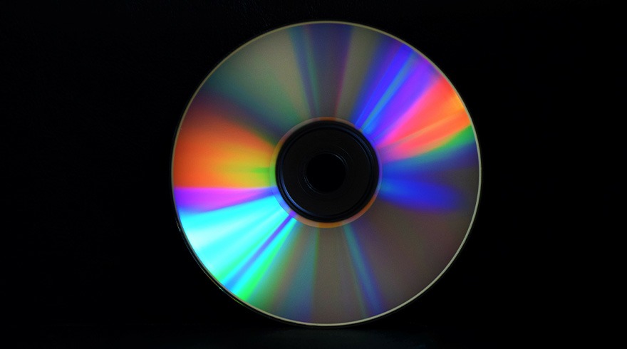 Een glanzende CD met regenboogkleuren ligt tegen een zwarte achtergrond, het midden is zwart.