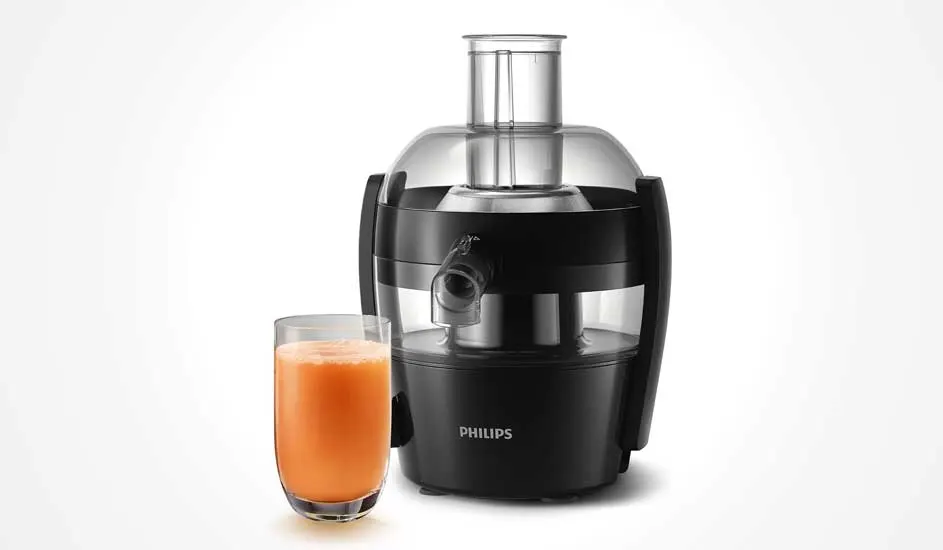 Une centrifugeuse presse des fruits en haut en jus rouge qui coule dans un verre, la pulpe est récupérée à part dans un récipient.