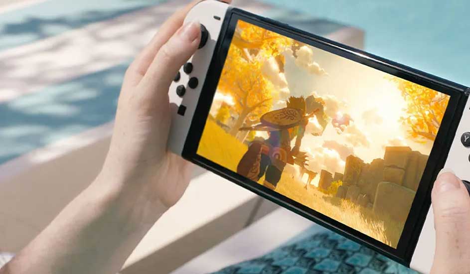 Une personne tient une Nintendo Switch près de la piscine, jouant à un jeu coloré avec un paysage ensoleillé à l’écran.