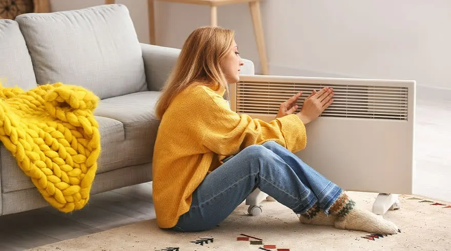 Une pièce avec un divan gris, un plaid jaune, et un radiateur blanc au sol, près d'un tapis à motifs géométriques.