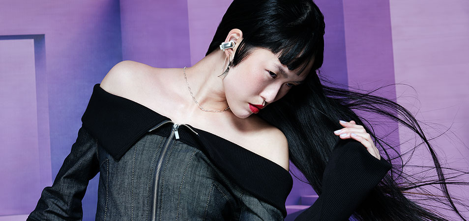 Een foto toont een grijs denim jasje met een zwarte kraag tegen een paarse achtergrond.