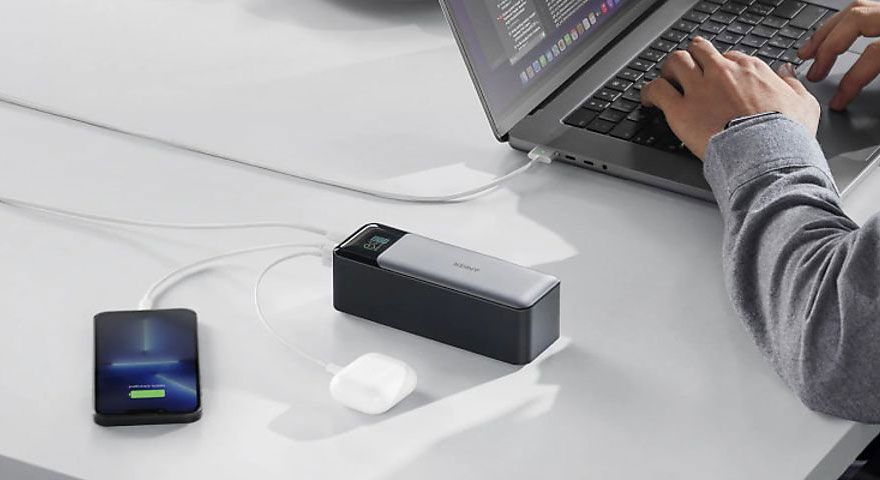 Ordinateur portable connecté à une batterie externe, avec un téléphone en charge à proximité.