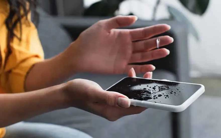 Une personne examine un smartphone mouillé avec des gouttes d'eau sur l'écran, peut-être après un accident avec du liquide.