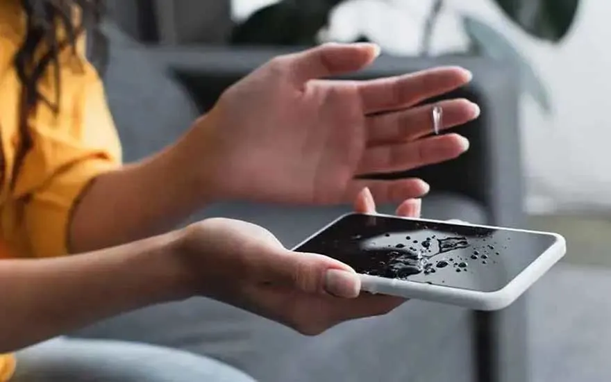 Een persoon bekijkt een smartphone met wat druppels water op het scherm, mogelijk is het toestel nat geworden door een ongelukje.