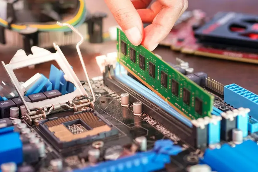 Een hand installeert een groene RAM-module in een computer moederbord met blauwe sloten.