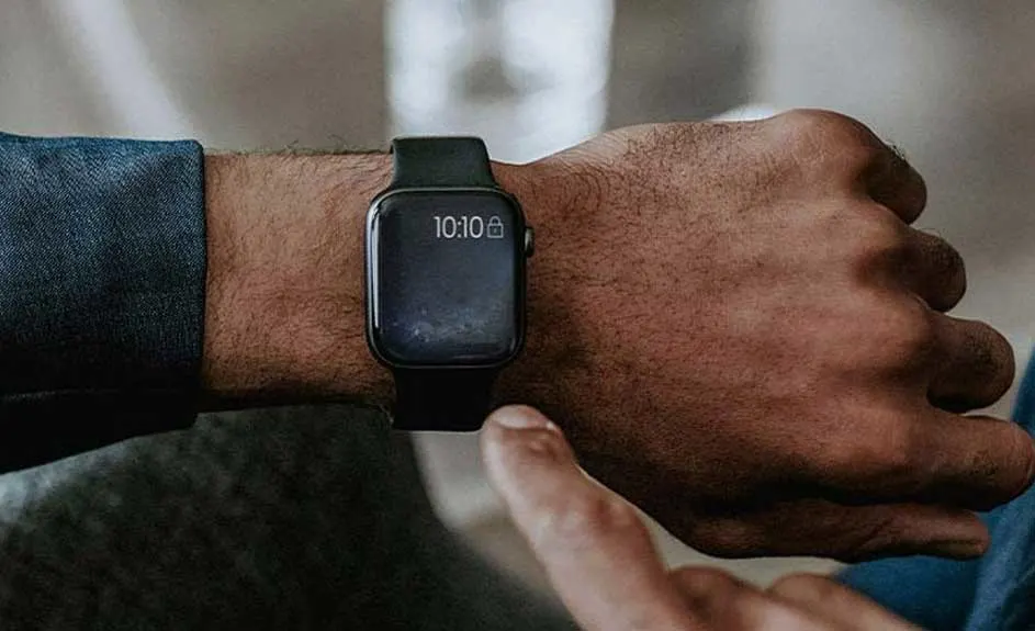 Een zwart horloge toont 10:10 op een pols. Een vinger raakt het scherm aan. Blauwe mouw gedeeltelijk zichtbaar.