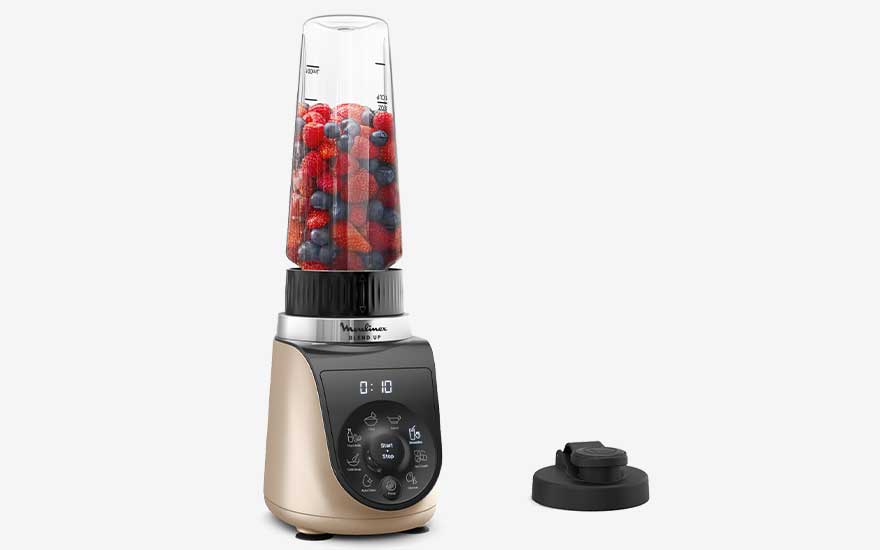 Un blender à commande digitale, garni de fruits rouges et de myrtilles, est présenté sur fond blanc.