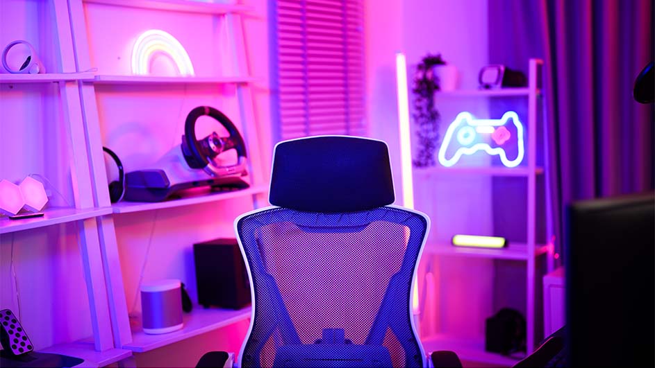 Een blauwe gamingstoel staat voor een bureau. Achter de stoel staan witte planken met een neoncontroller en een regenbooglamp.