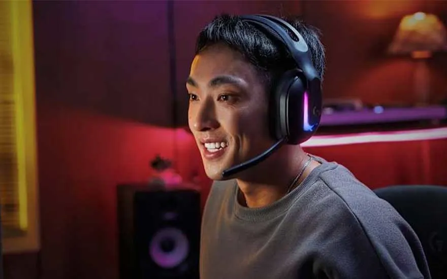 Een lachende gamer draagt een zwarte headset met paarse RGB-verlichting in een kleurrijke gaming-kamer met neonlichten op de achtergrond.