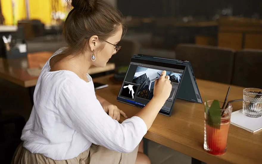 Vrouw werkt op laptop met stylus in café. Cocktail en notitieboekje op tafel. Achtergrond is vaag.