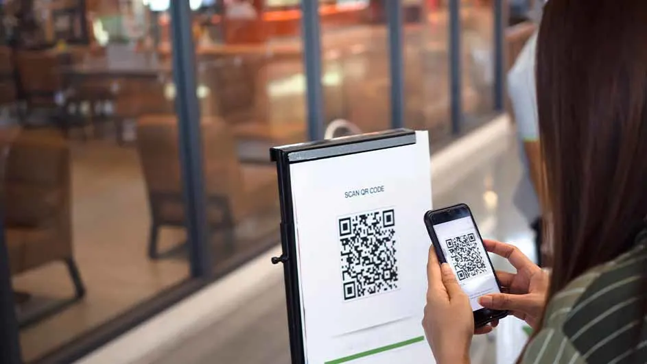 Une personne scanne un code QR sur un présentoir avec un téléphone. L'arrière-plan montre un intérieur de restaurant flou.