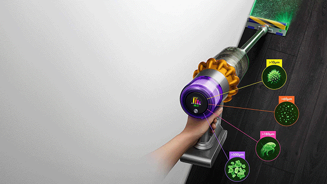 Un aspirateur violet dyson et or nettoie un sol foncé. Des cercles montrent des particules aspirées, sur un fond blanc.