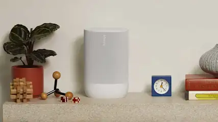 Étagère beige avec plante en pot orange, haut-parleur blanc, réveil bleu, livres et vase texturé.