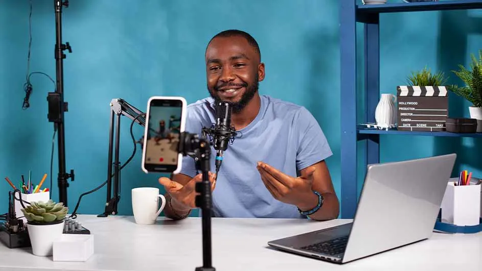 Un bureau blanc avec un ordinateur portable, un microphone, un téléphone et une tasse devant un fond bleu.