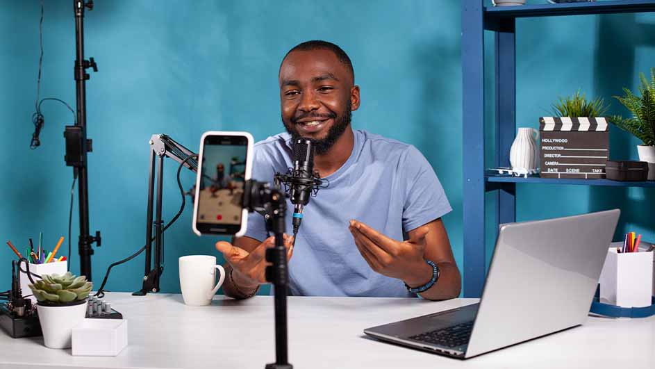 Un bureau blanc avec un ordinateur portable, un microphone, un téléphone et une tasse devant un fond bleu.