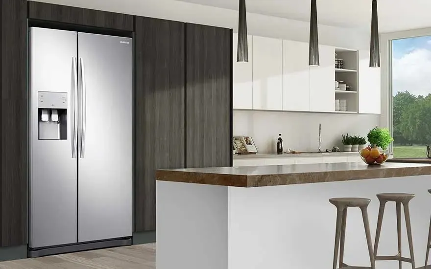 Un réfrigérateur argenté à quatre portes avec distributeur d'eau intégré dans une cuisine moderne aux tons neutres.