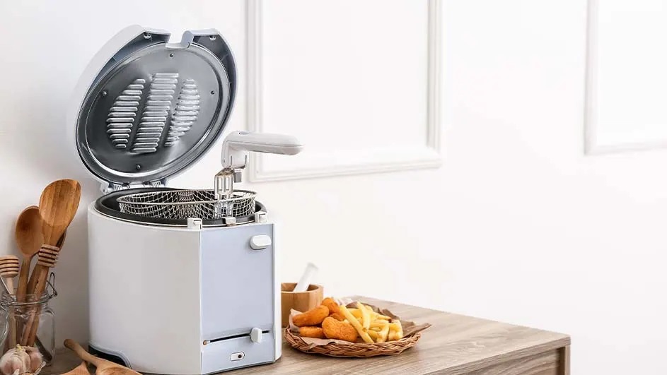 Een witte friteuse met open deksel staat op een houten tafel naast een mandje met snacks.