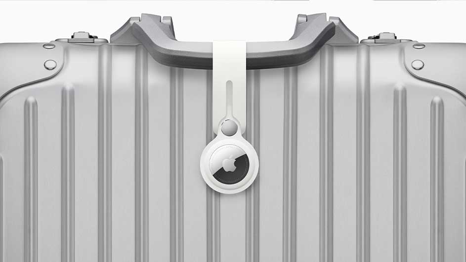 Valise argentée avec un AirTag blanc attaché à la poignée, sur fond blanc.
