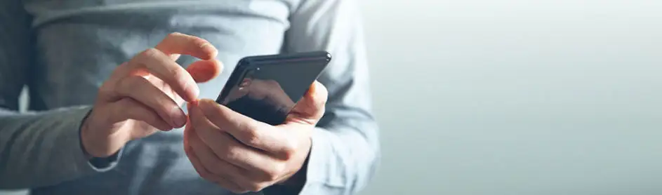 Gros plan sur des mains manipulant un smartphone noir devant un fond gris clair.
