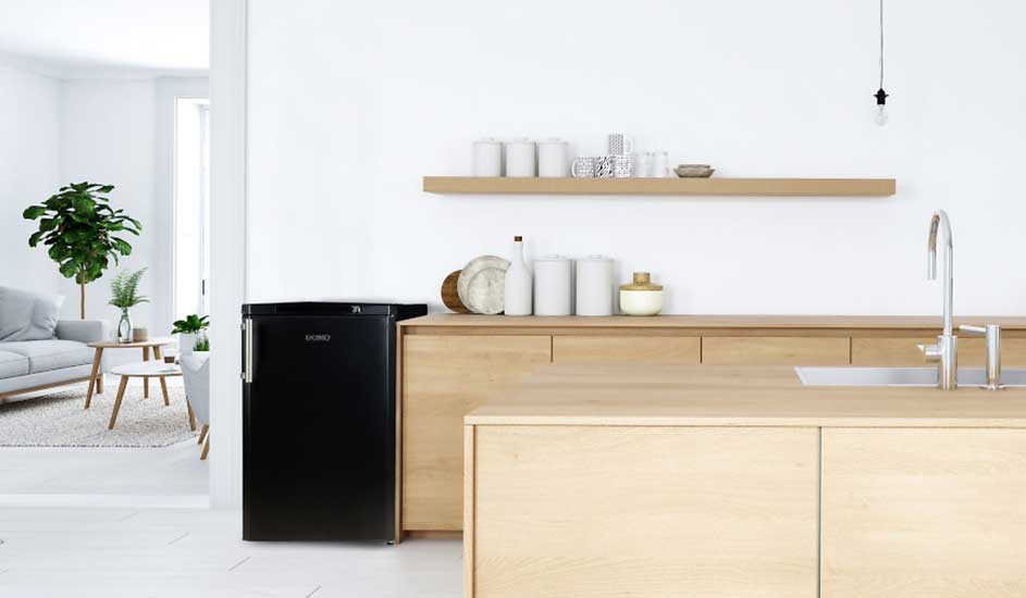 Intérieur minimaliste avec frigo noir, plan de travail en bois clair, étagères et évier. Plantes vertes et salon en arrière-plan.