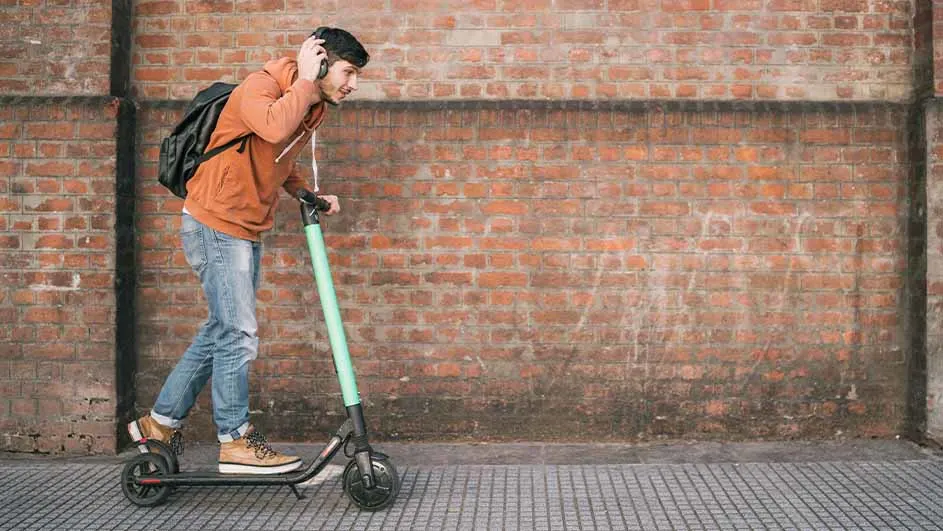 Een persoon op een groene step voor een bakstenen muur. De ondergrond is betegeld.