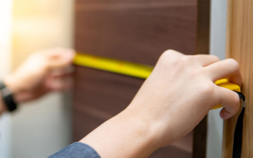 Main tenant un mètre ruban jaune contre une surface en bois brun pour mesurer.