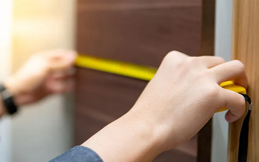 Main tenant un mètre ruban jaune contre une surface en bois brun pour mesurer.