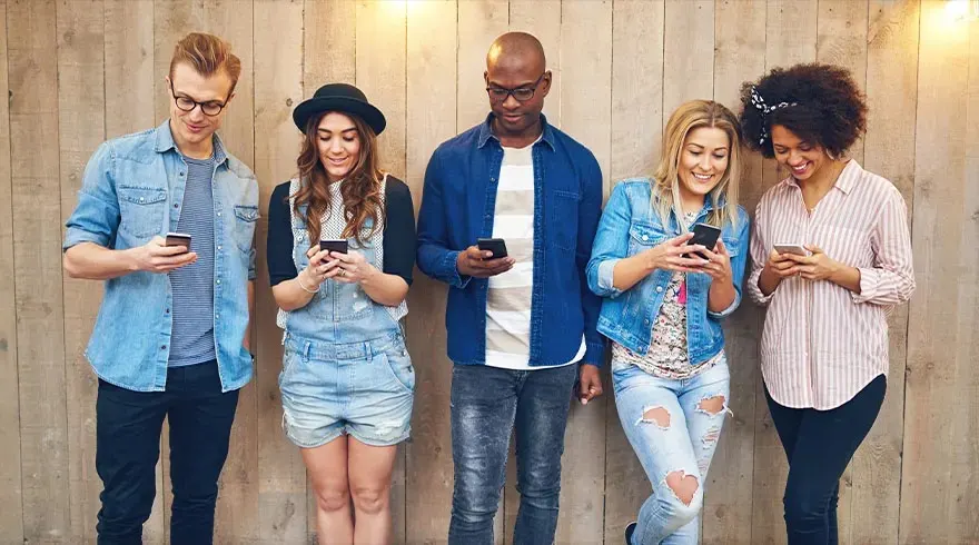 Cinq personnes devant un mur de bois utilisent des téléphones portables. Vêtements décontractés, jeans, denim. Lumière douce en haut.