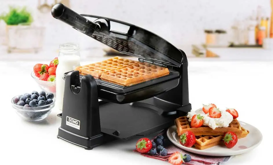 Een wafelijzer met wafels, geserveerd met aardbeien, blauwe bessen en slagroom. Een fles melk staat ernaast.