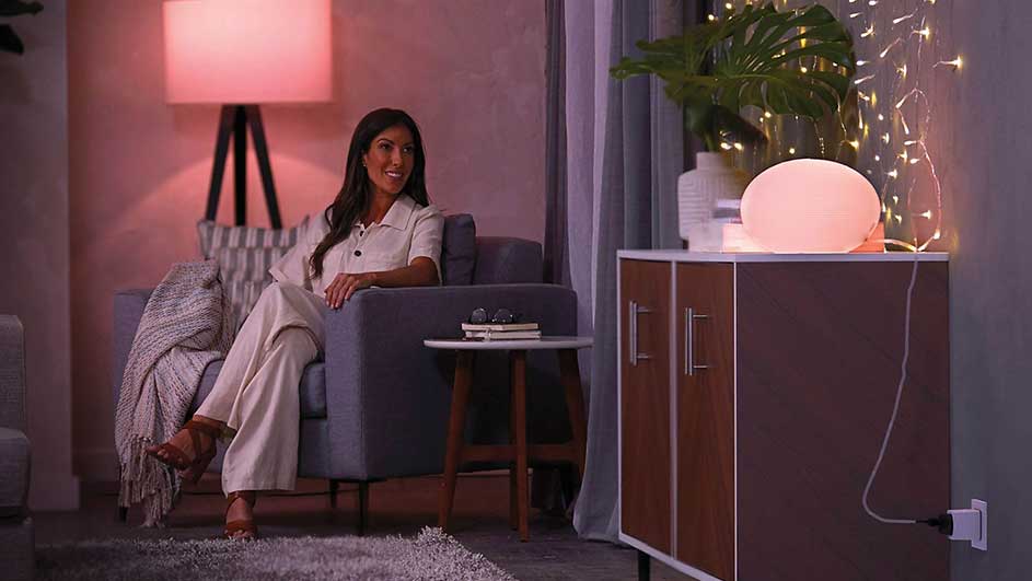 Salon éclairé avec fauteuil gris, table d'appoint, armoire à deux portes, guirlande lumineuse et lampe de sol.