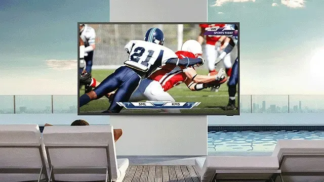 Une grande télévision montre un violent plaquage de football américain dans un espace luxueux avec vue sur une piscine et la ville.