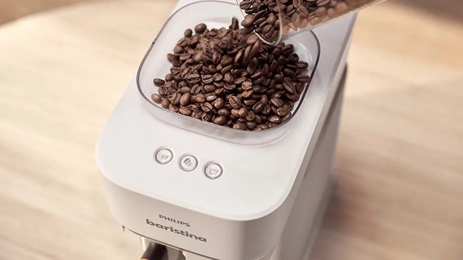 Bruine koffiebonen worden in een transparant reservoir van een witte Philips Baristina-koffiemachine gegoten.