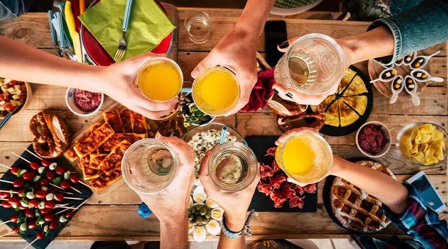 Vue aérienne d'une table en bois avec des boissons levées au-dessus de divers plats et amuse-gueules.