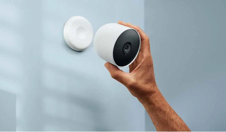 Een hand plaatst een witte Google Nest Cam tegen een lichtblauwe muur, vlakbij de ronde magneetbeugel. Modern en minimalistisch ontwerp.