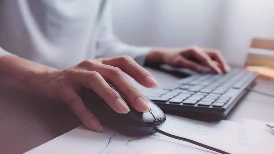 Een close-up van handen die een zwarte computermuis en een toetsenbord bedienen op een bureau met papieren.