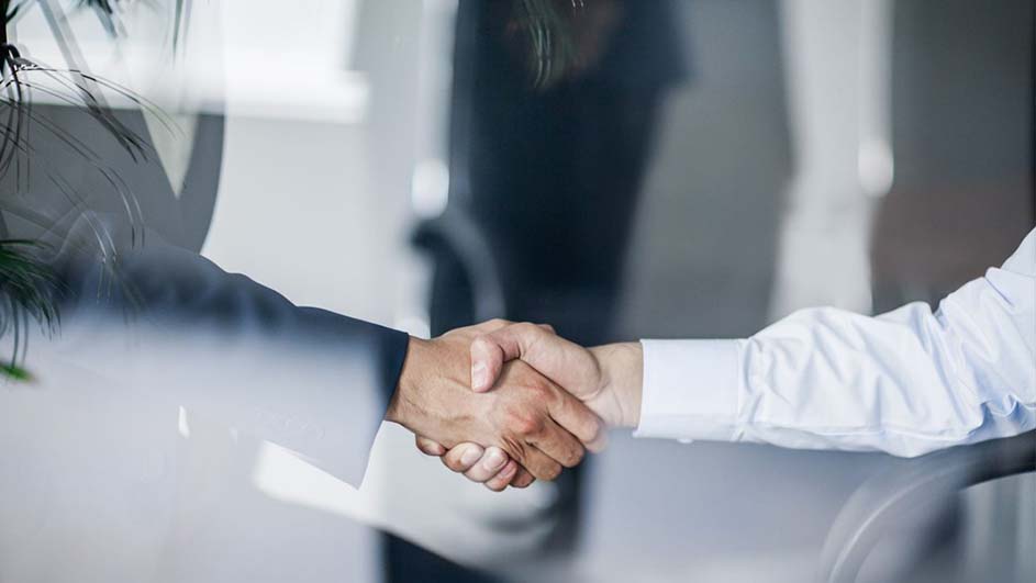 Twee handen schudden elkaar voor een vage, lichte achtergrond. Een mouw is donker, de ander wit.